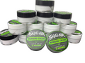A stack of small white plastic jars of Skullair Tattoos Numbing Cream with black lids, arranged on a dark textured surface. Two jars in the front have green and black labels showing the brand name and product details.